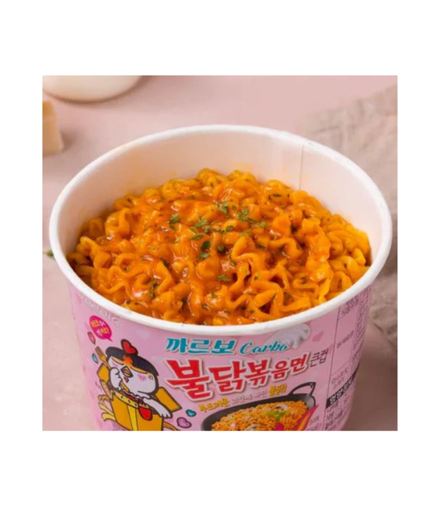 Open pink Buldak Carbonara cup with orange noodles and herbs garnish